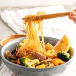 chopsticks lifting shirataki noodles covered in stir fry sauce with veggies in a bowl