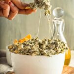 spinach artichoke dip being scooped up from a bowl with strings of cheese