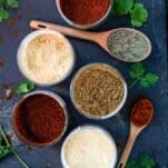 containers with taco seasoning and wooden spoons on a black board with cilantro all around