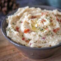 bowl of cauliflower mash with bacon bits, creamy butter and parsley