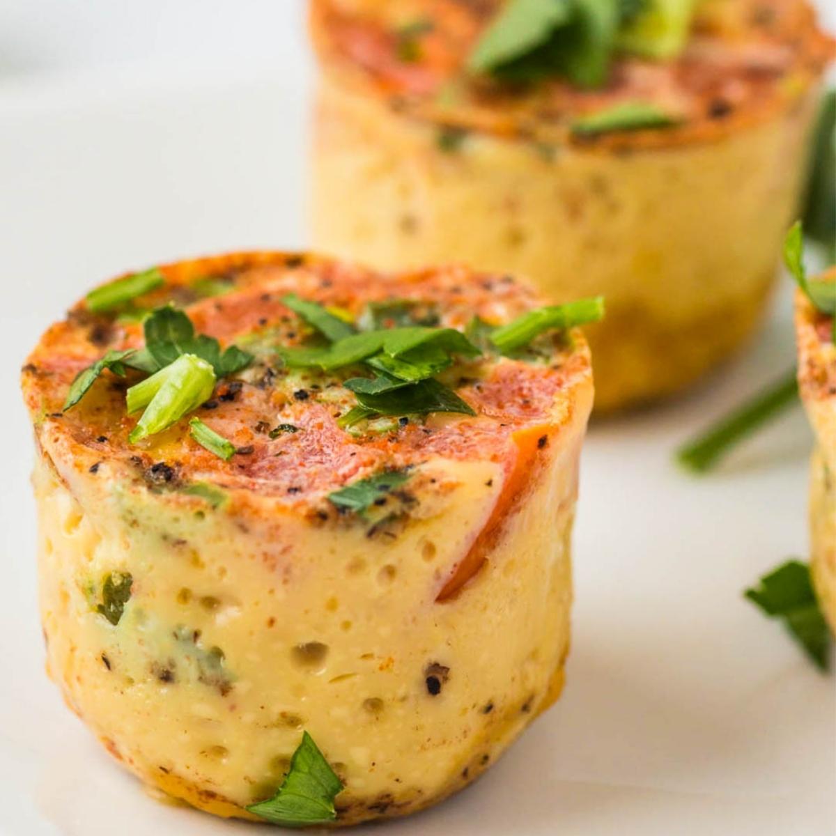 side view of an egg bite with cheese, peppers and seasonings topped with green onion